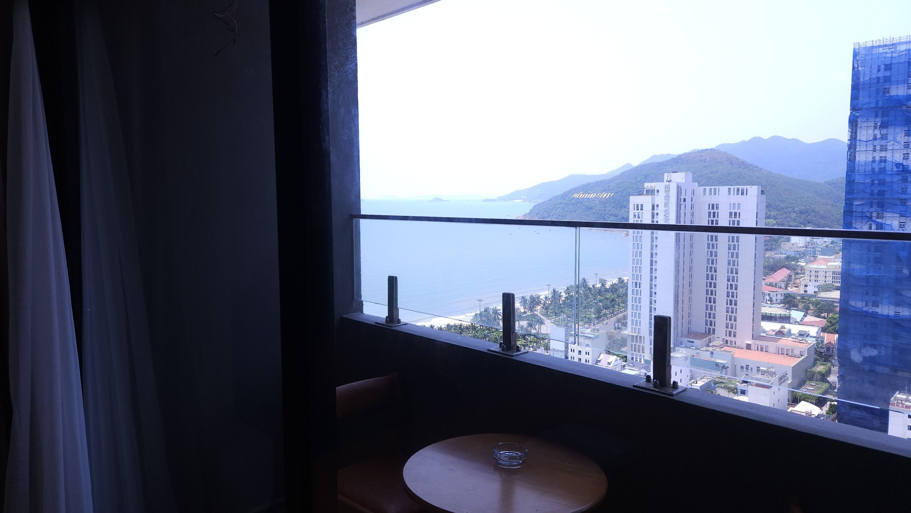 A room with a view of a coastal cityscape, including high-rise buildings and mountains.