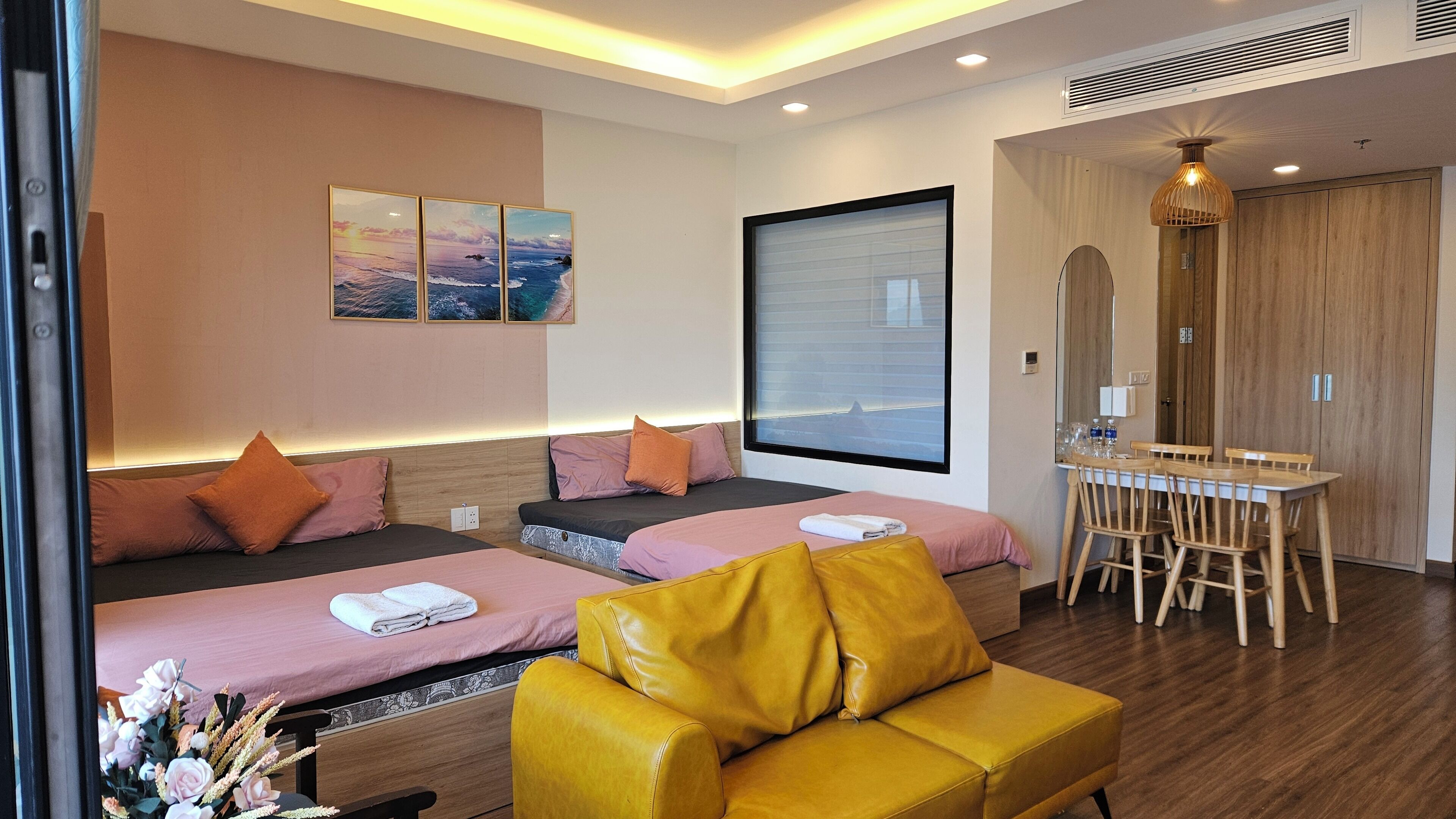 Ein Hotelzimmer mit zwei Betten, einem Holztisch, einem gelben Sessel und einem großen Fenster.