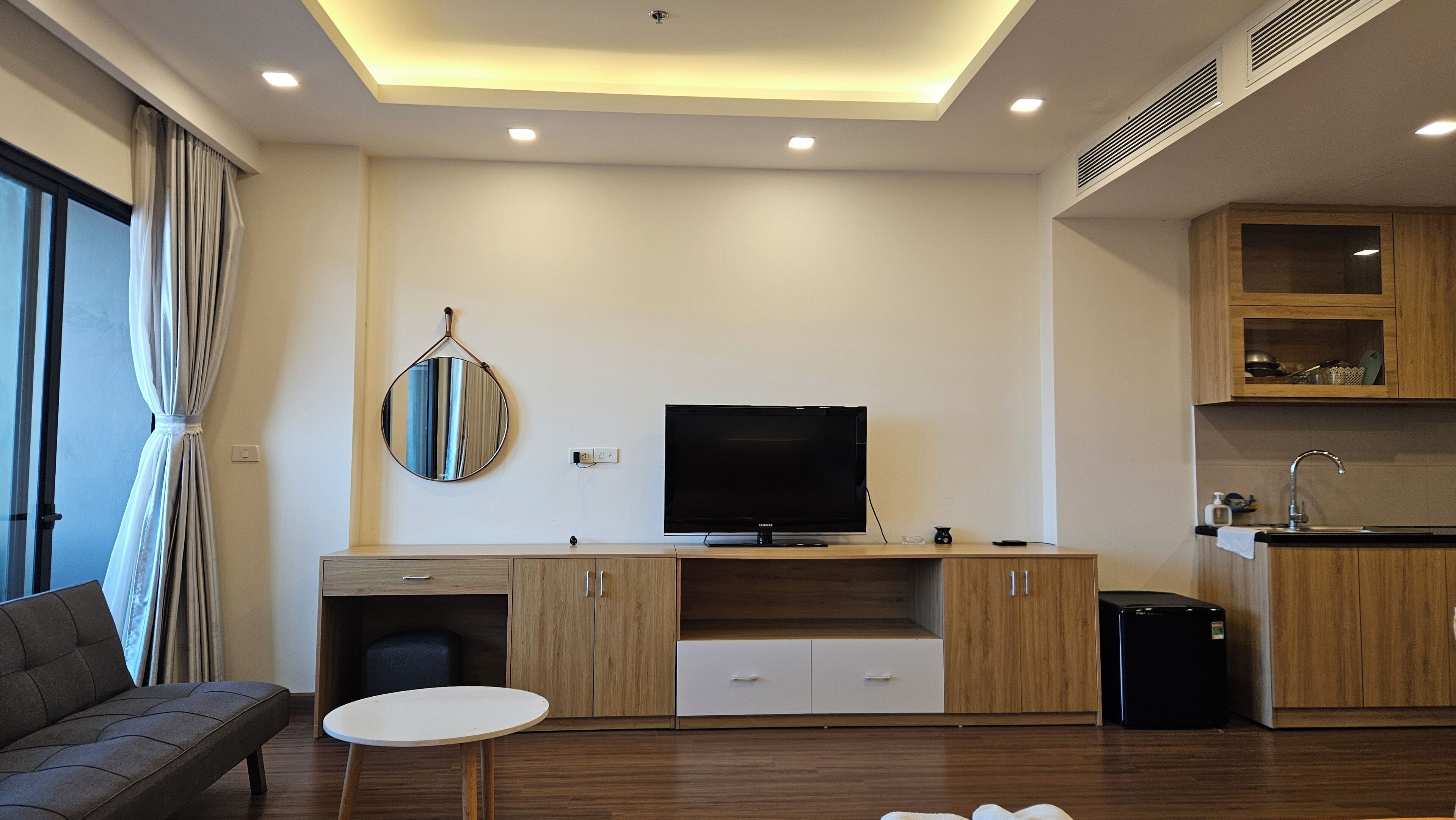A modern living room with a flat-screen TV, wooden cabinets, a small table, and a sofa.
