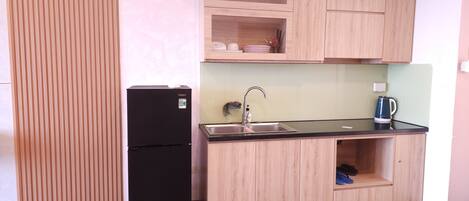 Una cocina compacta con un refrigerador negro, un lavamanos y una cafetera.