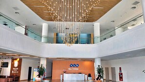 Un hall d’hôtel moderne avec un comptoir d’accueil central, des espaces de détente et un luminaire décoratif au plafond.