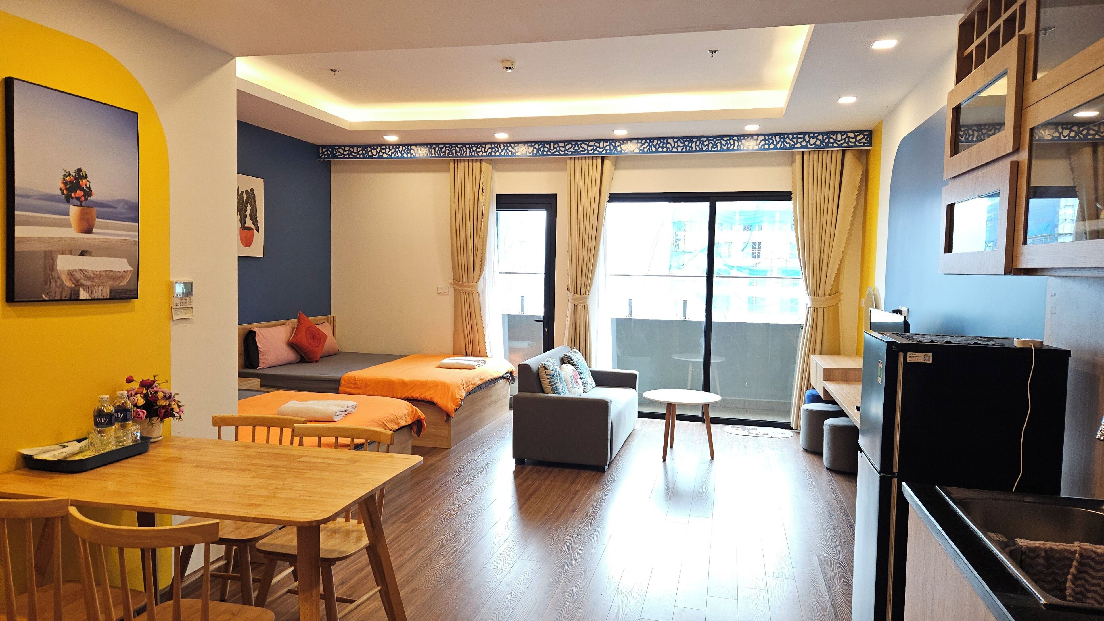 A hotel room with two beds, a sofa, a small table, and a kitchenette.