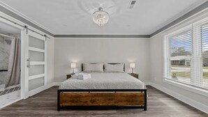 A bedroom with a large bed, two bedside lamps, a chandelier, and a view through the window.