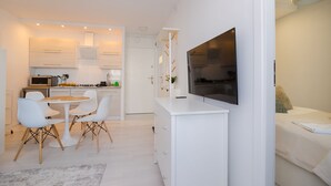 A modern kitchen with white cabinetry, a dining area with a round table and chairs, and a TV mounted on the wall. - ShortStayPoland Batorego B139 (Warsaw)