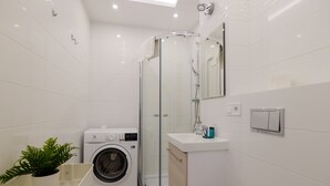 A modern bathroom with a glass-enclosed shower, a washing machine, and a sink with a mirror. - ShortStayPoland Batorego B139 (Warsaw)