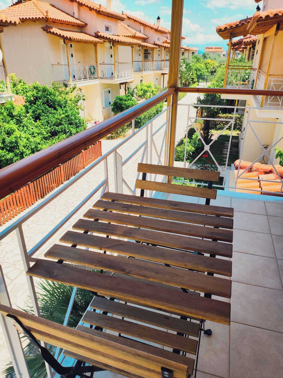 A wooden staircase with a metal railing leading to a balcony with a view of a residential area.