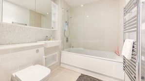 Ein modernes Badezimmer mit einer gläsernen Duschkabine, einer Badewanne, einer Toilette und einem Waschtisch mit Spiegel.