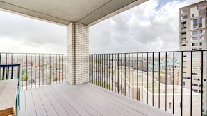 Ein Balkon mit Blick auf eine Stadtlandschaft, mit einer Ziegelstütze und einem Metallgeländer.