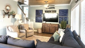 Un salon avec un plafond en bois, un téléviseur à écran plat, un canapé, un fauteuil et un escalier.