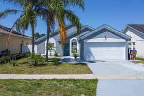 A modern single-story house with a garage, a front yard with palm trees, and a clear blue sky.