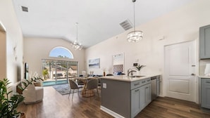 A spacious kitchen with a large island, modern pendant lights, and a view to a dining area. - 8615 Vacation Oasis House Private Pool Grill (Kissimmee)