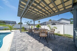 An outdoor patio with a pool, wicker furniture, and a covered area with string lights.