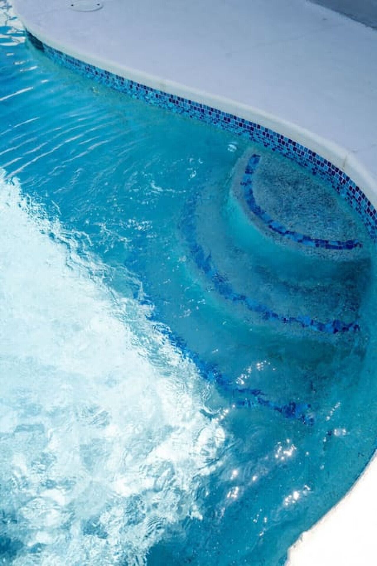 A swimming pool with clear blue water and a tiled edge.