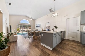 Una cocina amplia con una isla grande, modernas lámparas colgantes y vistas a un comedor.