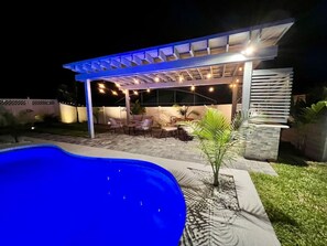 A covered outdoor seating area with a pool, surrounded by a well-maintained lawn and a small palm tree.