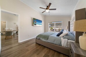 A bedroom with a bed, a ceiling fan, a painting, and a view through a window.