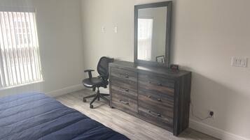 A bedroom with a bed, a dresser, a chair, a mirror, and a window with blinds.