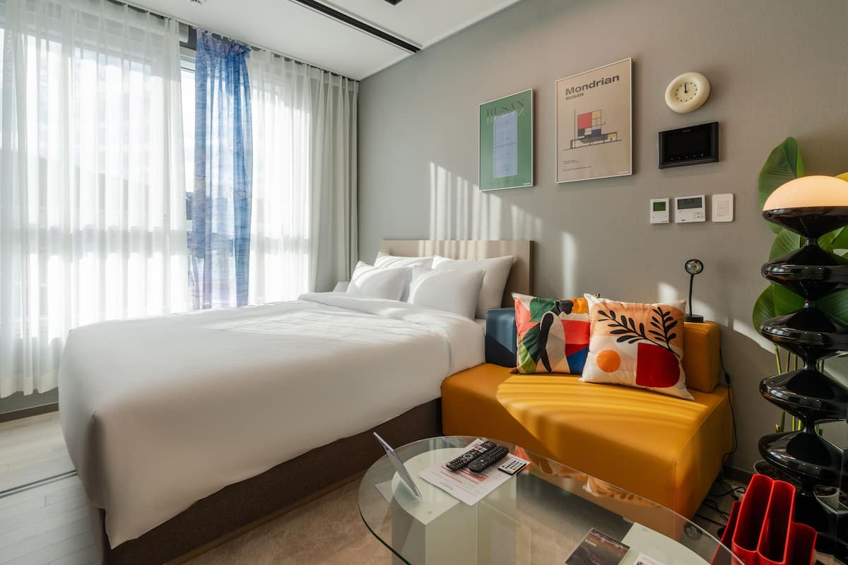 Habitación de hotel con una cama grande, una mesita de noche con una lámpara, una mesita auxiliar con un ordenador portátil y un reloj en la pared.