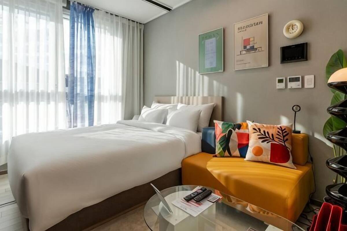 Habitación de hotel con cama, sofá, mesa de centro de vidrio y vista panorámica de la ciudad.