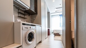 A modern laundry room with a front-loading washing machine, a built-in dryer, and a microwave. - Radiant Nampo Hotel (Busan)