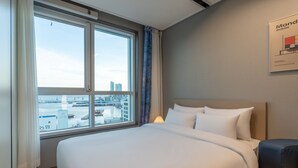 A hotel room with a large bed, a view of the city through a window, and a framed picture on the wall. - Radiant Nampo Hotel (Busan)