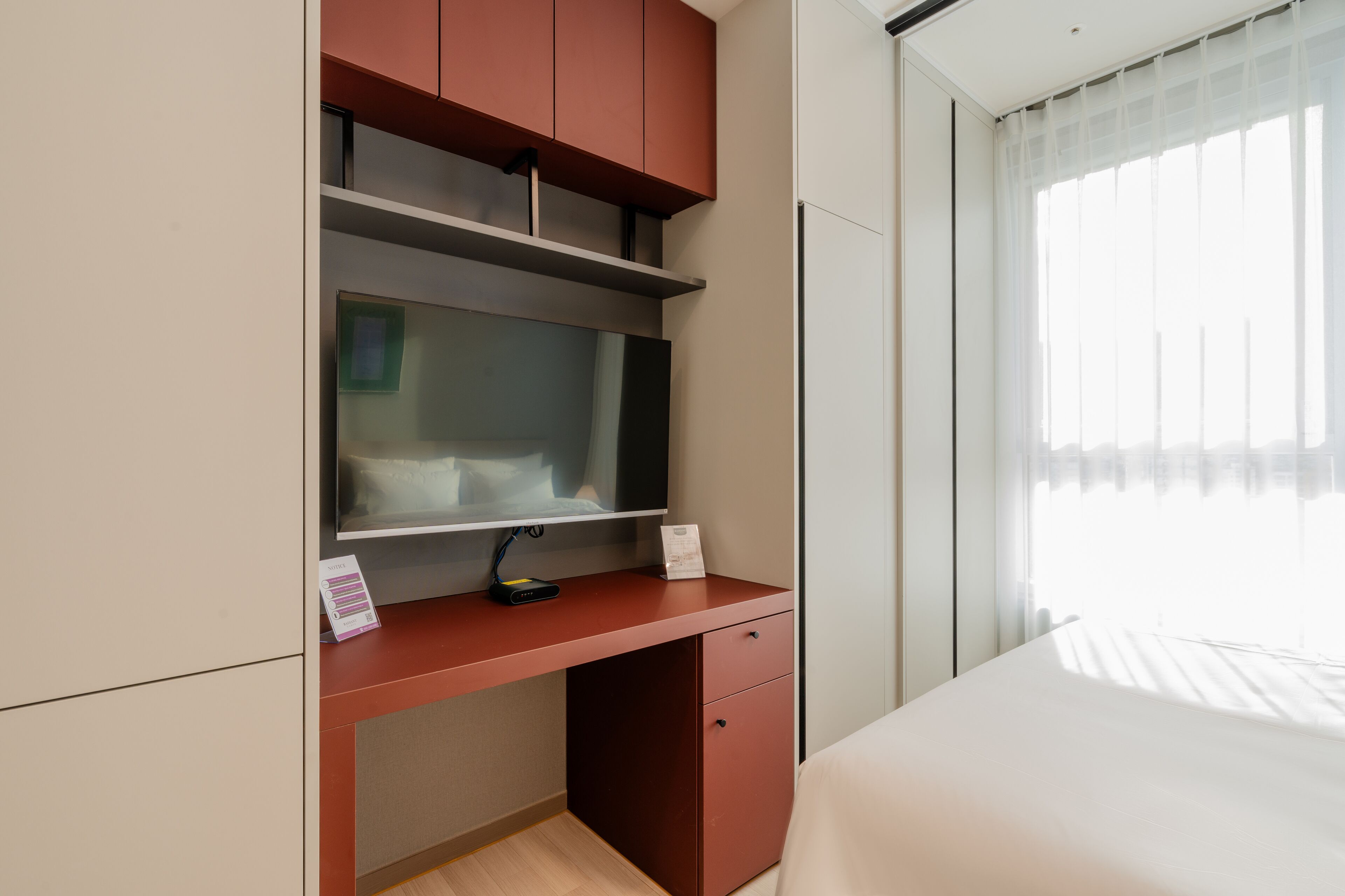 Moderni hotellihuone, jossa on työpöytä, sänky ja ikkuna, jossa on läpikuultavat verhot.