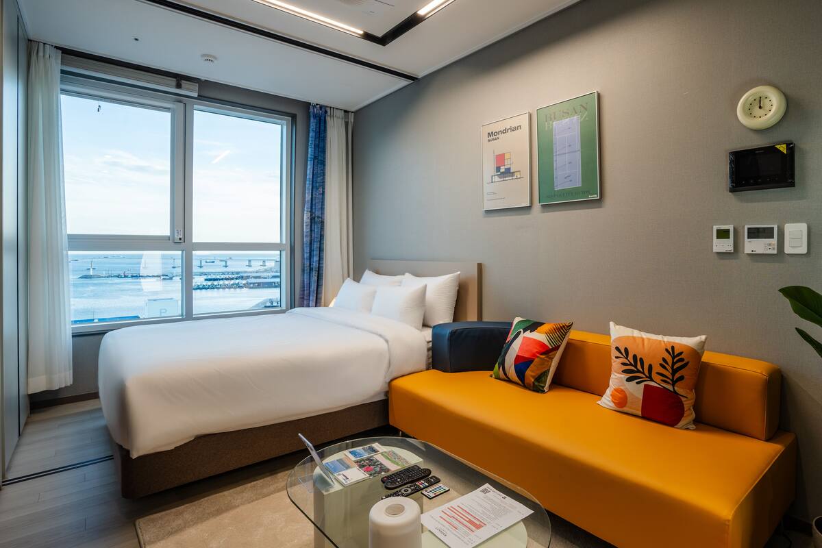 Habitación de hotel con cama, sofá, una mesita de cristal y vistas al mar.