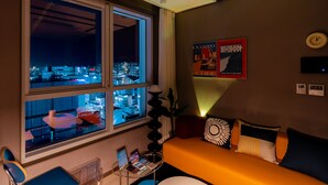 A hotel room with a large window, a bed with orange bedding, a desk with a chair, and a plant. - Radiant Nampo Hotel (Busan)