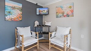 A corner room with two white cushioned chairs, a TV mounted on the wall, and two paintings depicting beach and coral scenes. - King Room Hotel- 2 Pools, Near Beach/Boardwalk, No Pets Allowed (Carolina Beach)