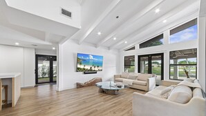 Ein geräumiges Wohnzimmer mit einem großen Glastisch, einem beigen Sofa und einem großen Fenster mit Blick ins Freie.