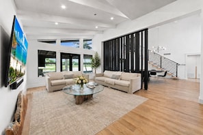 A spacious living room with a large glass coffee table, two sofas, and a staircase leading to an upper level.