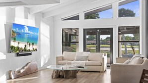 Ein modernes Wohnzimmer mit einem Glastisch, einer Couch und Blick auf einen Strand durch große Fenster.