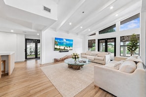A spacious living room with a glass coffee table, a sofa, and a TV mounted on the wall.