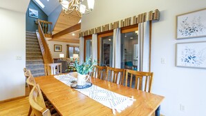Un espace repas comprenant une table en bois, des chaises, un lustre et un escalier.