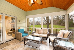 A covered porch with wicker furniture, a glass table, and a view of the outdoors.