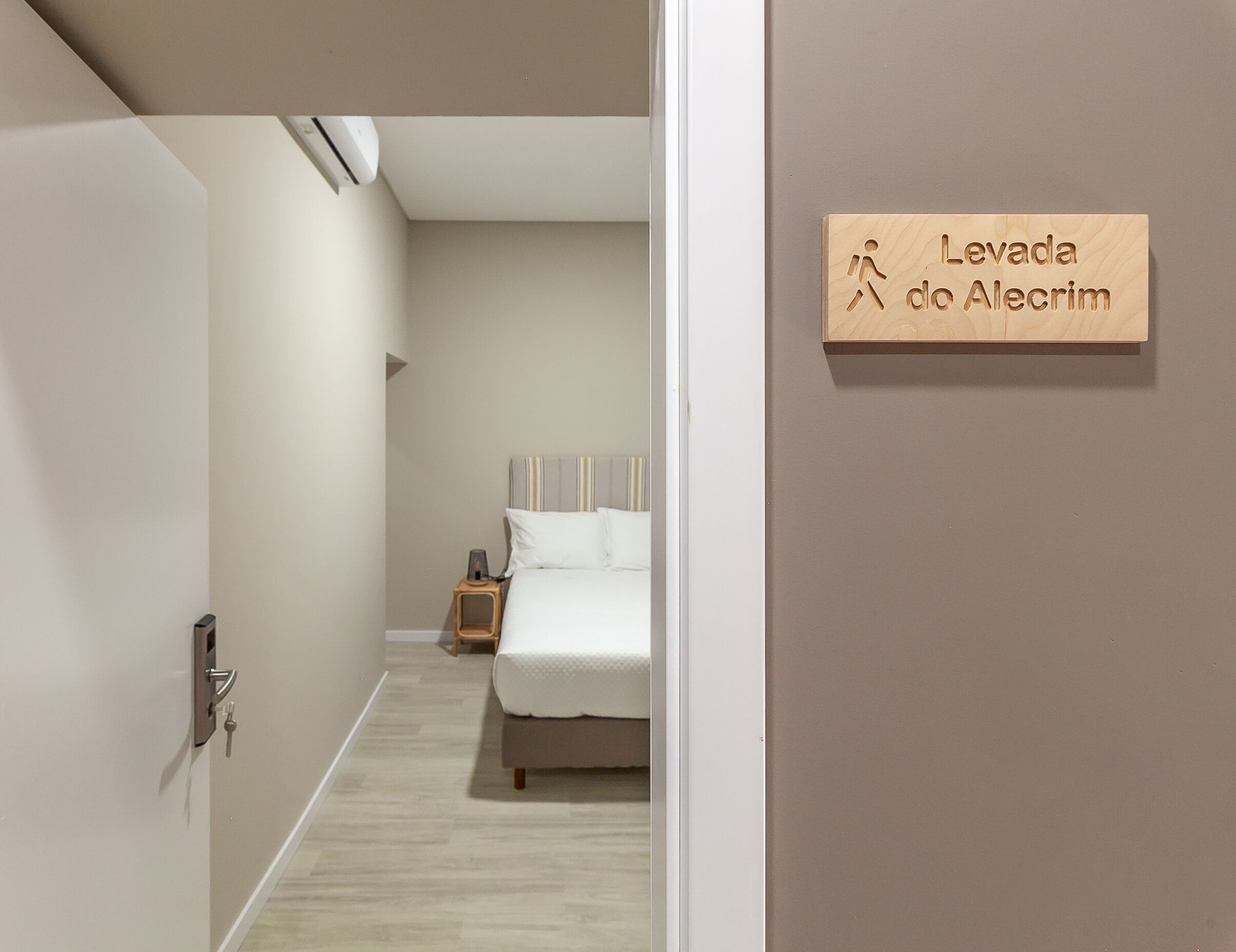 A hotel room with a bed, a nightstand, and a sign reading "Levada do Alecrim".