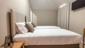 Cama doble con edredón blanco acolchado, mesita de noche con lámpara y televisor montado en la pared.