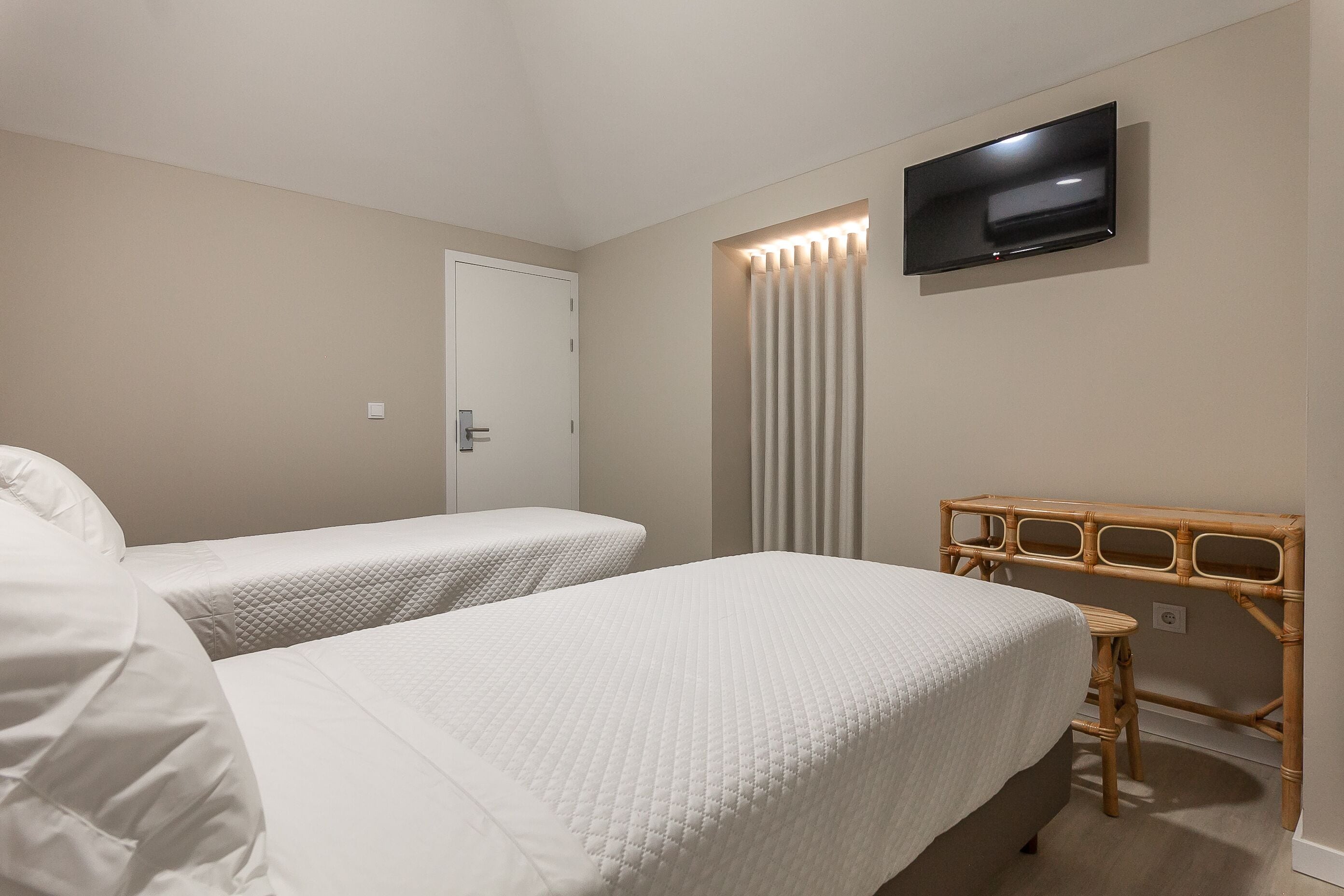 Une chambre d’hôtel avec deux lits, un téléviseur fixé au mur et un bureau en bois.