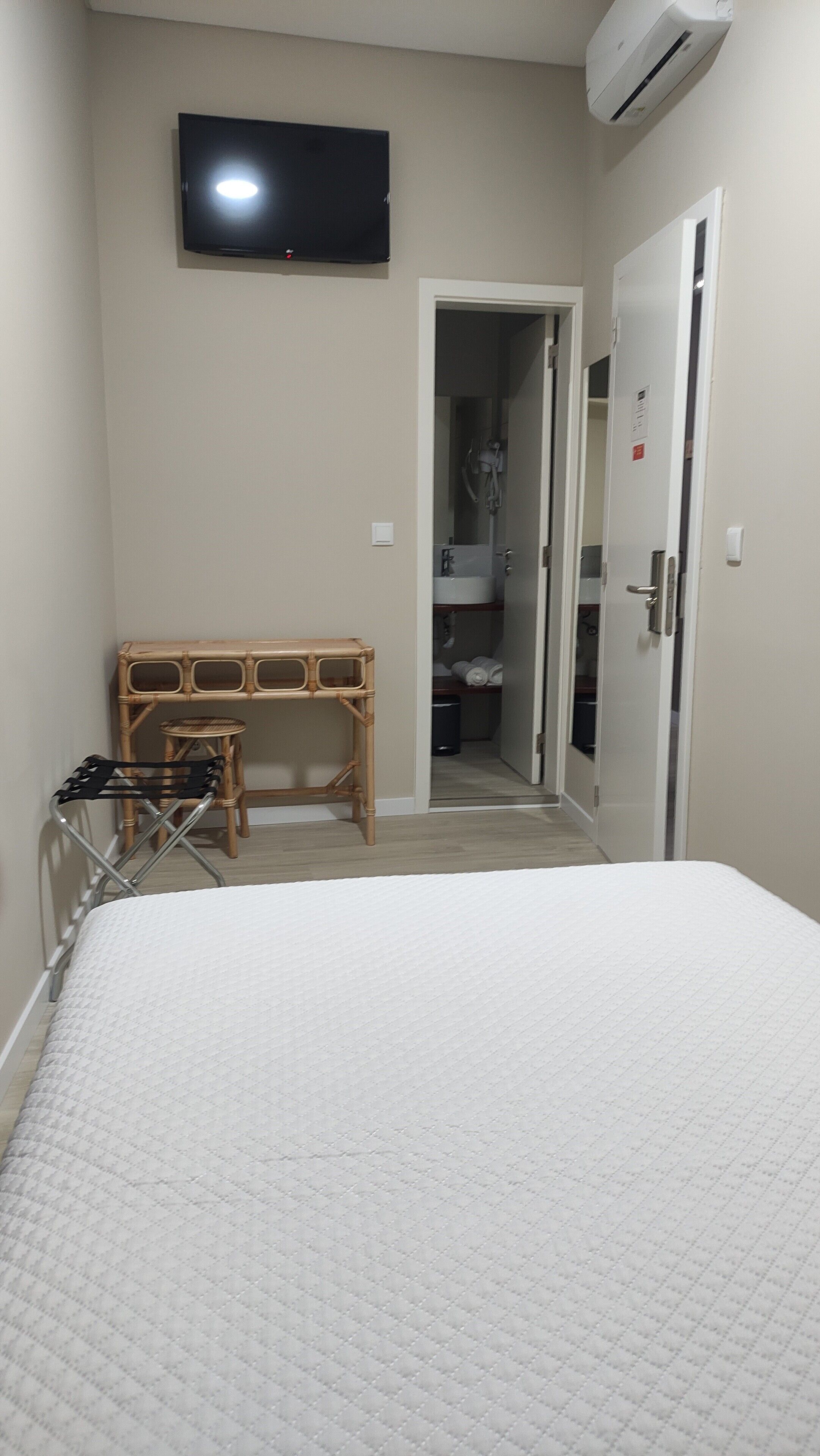 Una camera da letto con un letto, una televisione montata a parete, un condizionatore, un armadio e un bagno visibile attraverso una porta aperta.