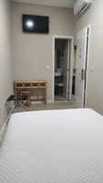 Una camera da letto con un letto, una televisione montata a parete, un condizionatore, un armadio e un bagno visibile attraverso una porta aperta.