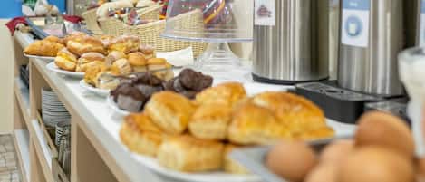 Ein Buffet mit verschiedenen Gebäcksorten, Kaffeeautomaten und einem an der Wand befestigten Fernseher.