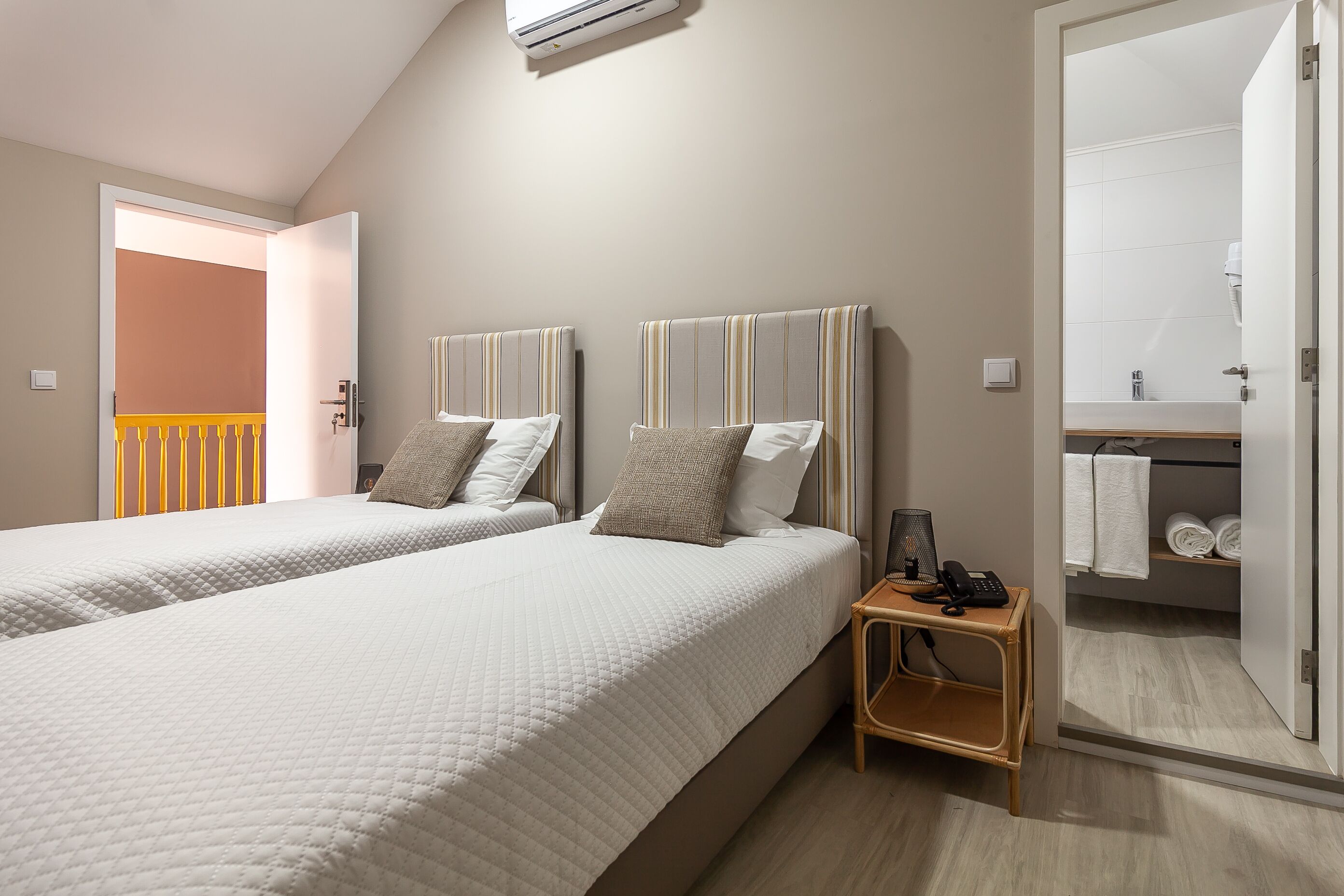 Habitación de hotel con dos camas, una mesita de noche con teléfono, y un baño visible a través de una puerta abierta.