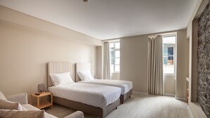 Quarto com duas camas, mesa de cabeceira, cadeira e parede com detalhes em pedra.