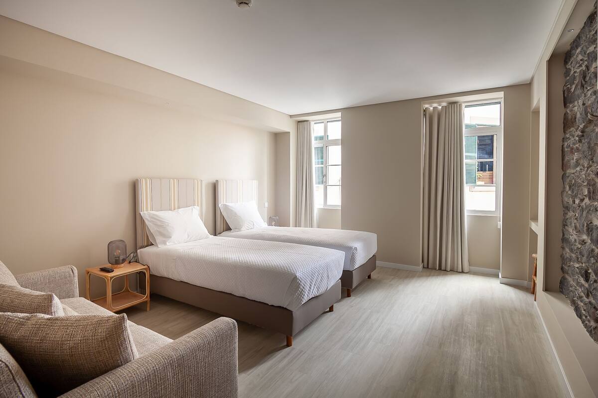 Un dormitorio con dos camas, una mesita de noche, una silla y una pared decorativa de piedra.