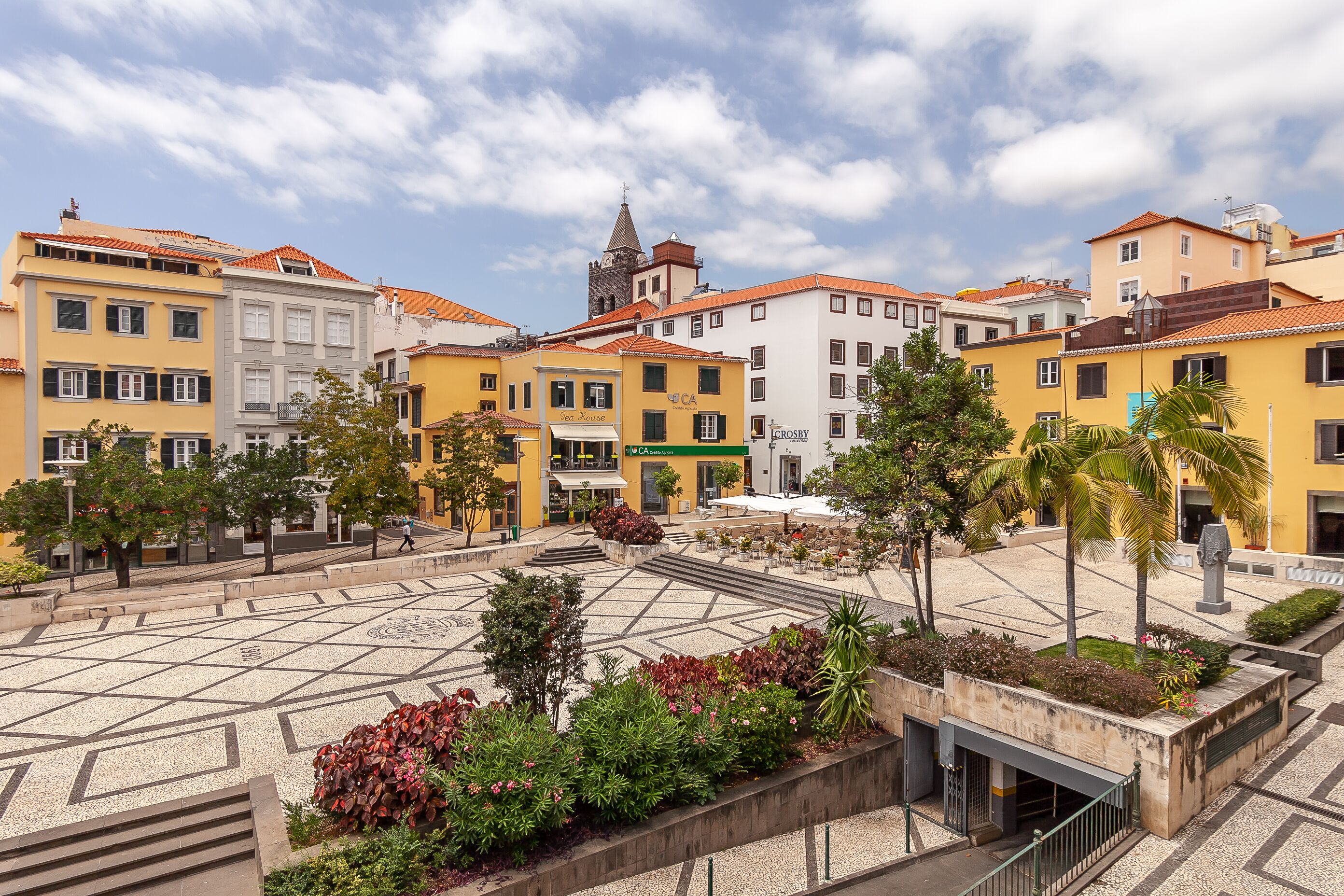 A plaza with buildings, a church tower, and a café.