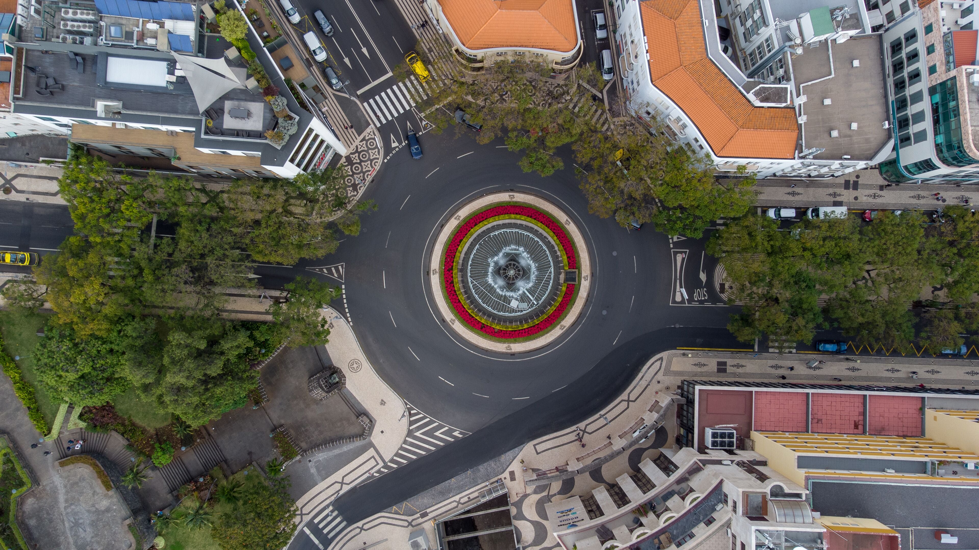 An aerial view of a roundabout with a central island, surrounded by buildings and greenery.