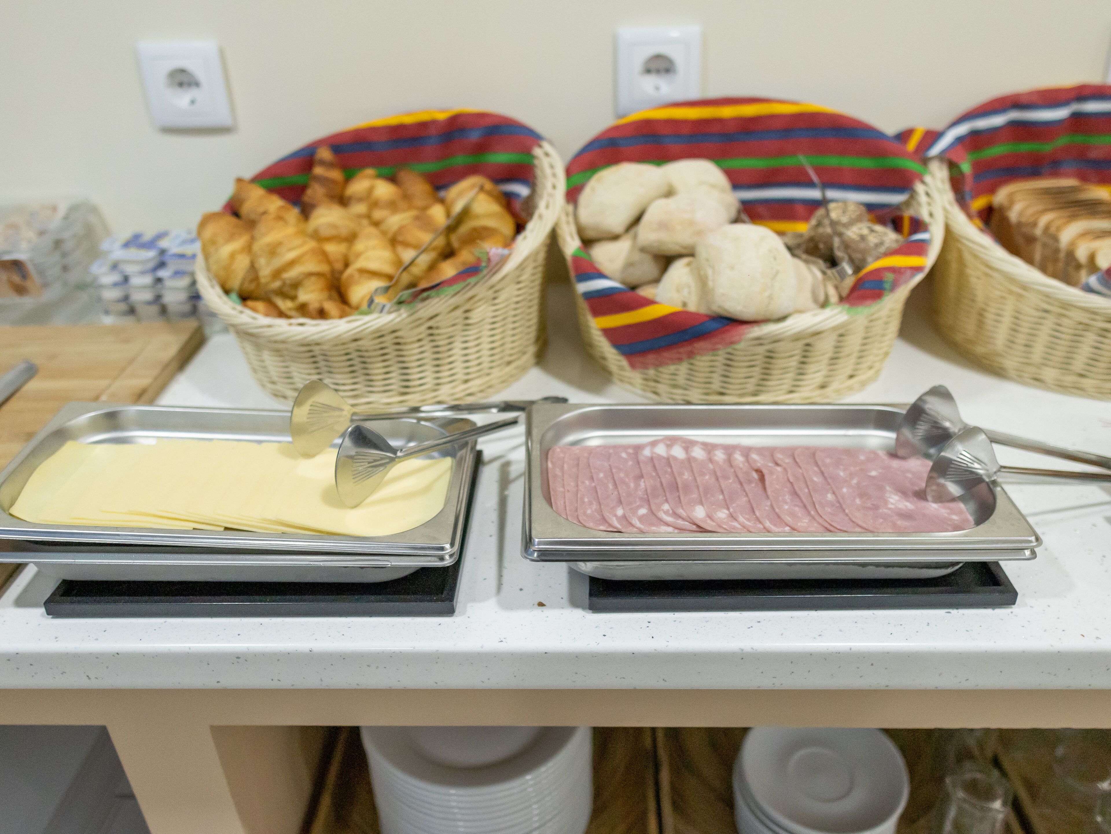 Un tavolo da buffet con piatti di burro, prosciutto a fette e cestini di pane e funghi.