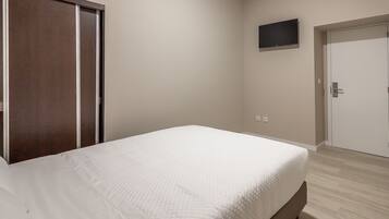 Un dormitorio con cama, armario, puerta y televisor en la pared.
