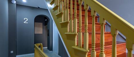 Una escalera con balaustres de madera y barandilla, que lleva a un rellano con una puerta marcada con el número 2.