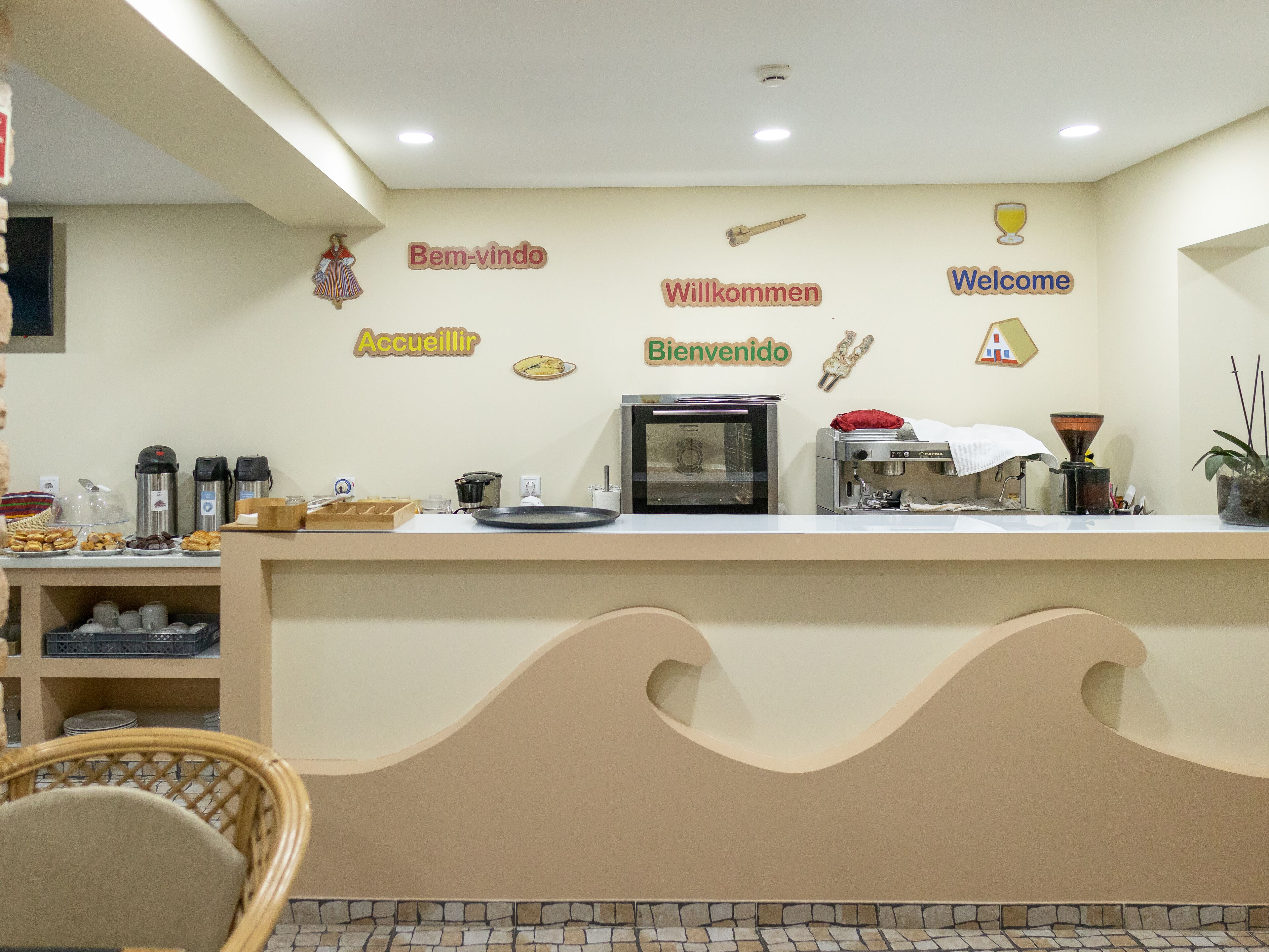 Ένας χώρος υποδοχής με πάγκο για καφέ, πολύγλωσσες πινακίδες καλωσορίσματος και μια περιοχή με καθίσματα, όπου υπάρχει μια καρέκλα από μπαμπού.